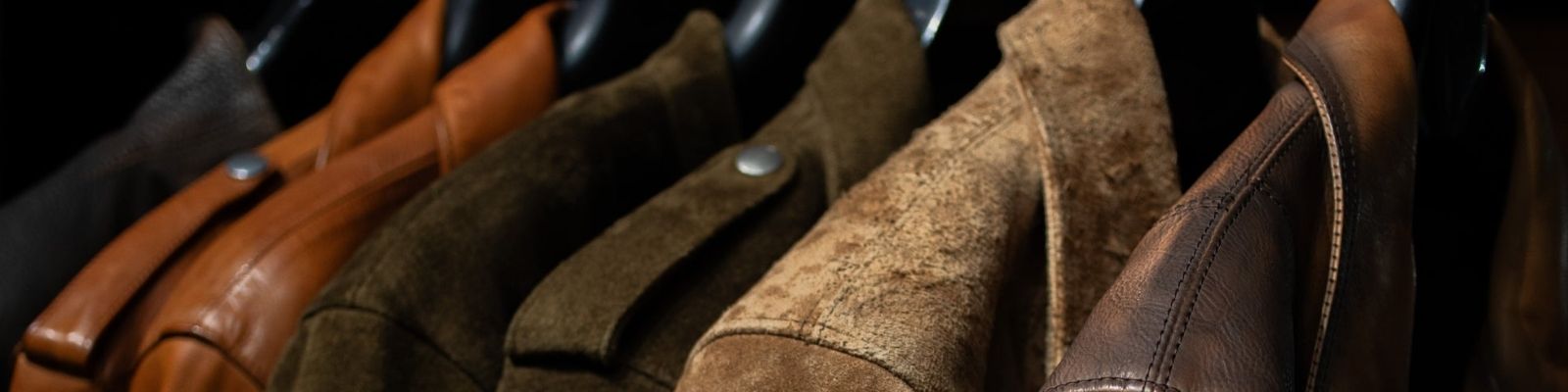 A close-up row of brown leather and suede jackets hanging on a rack, showing different textures and shades from dark brown to tan.